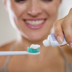 A woman applying toothpaste to a toothbrush.
